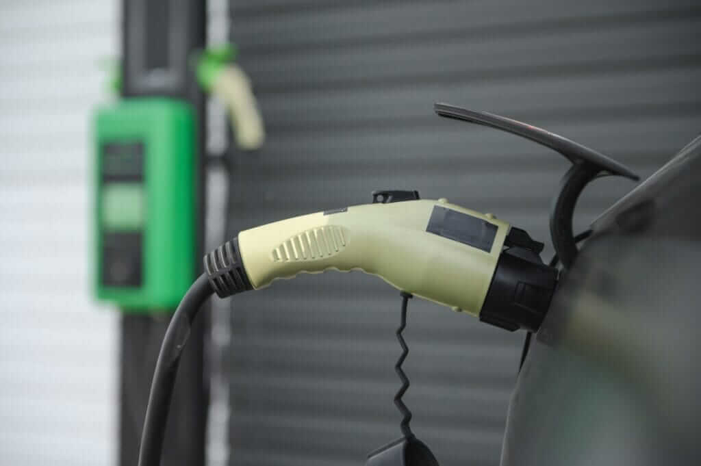 EV charging connector plugged into a car beside a wall-mounted charge point